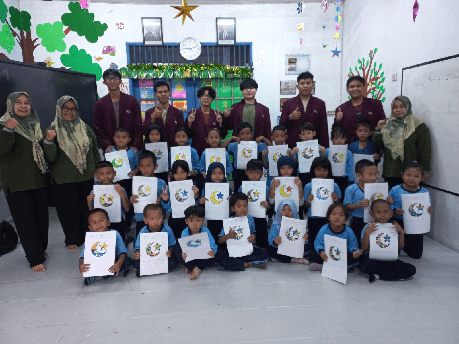 Volunteers, teachers, and children holding their artwork at PAUD Kenanga Asri.
